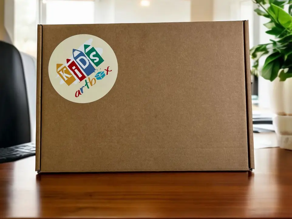 Ein brauner Versandkarton mit dem KIDSartbox Kleber am Deckel steht auf einem braunen Parkettboden.