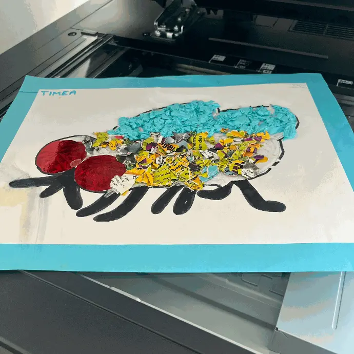 KIDSartbook Profi-Scan Eine bunte selbst gebastelte Kinderkunstfliege ist auf einem A3 Papier drappiert, das wiederum auf einem Flachbrettscanner liegt.